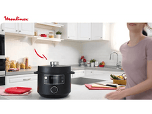 Charger l'image dans la galerie, Une femme passe devant une autocuiseur noir sur un comptoir de cuisine. Le logo Moulinex est visible.