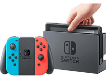 Charger l'image dans la galerie, Une console Nintendo Switch avec manettes Joy-Con détachées. Une main insère la Switch dans son dock.