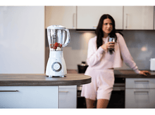 Charger l'image dans la galerie, Mixeur blanc avec fraises rouges et banane sur comptoir. Femme en arrière-plan.