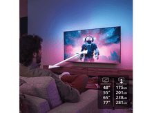 Charger l'image dans la galerie, Homme regardant la TV. TV montre un astronaute dans l'espace. Tailles TV de 48 à 77 pouces.