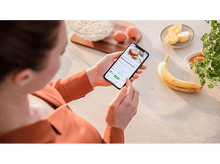 Charger l'image dans la galerie, Une femme tenant un téléphone avec une recette, avec de la nourriture autour.
