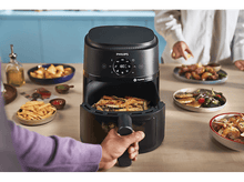 Charger l'image dans la galerie, Une friteuse à air avec de la nourriture à l'intérieur et des personnes en arrière-plan préparant d'autres plats.