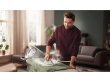 Charger l'image dans la galerie, Homme repassant un vêtement vert sur une planche. La vapeur s'élève du fer à repasser.