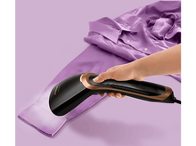 Charger l'image dans la galerie, Main repassant une chemise violette avec un défroisseur Philips, détails dorés, sur fond violet.