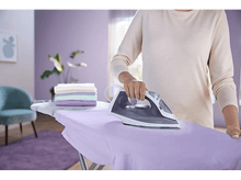 Charger l'image dans la galerie, Une personne repassant une chemise sur une table à repasser avec des vêtements pliés.