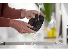Charger l'image dans la galerie, Mains lavant un appareil noir sous l'eau courante dans un évier, nettoyant un appareil.