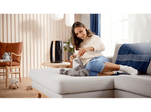 Charger l'image dans la galerie, Une femme joue avec un chat sur un canapé près d'un purificateur d'air noir.