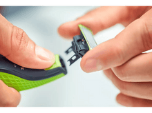 Charger l'image dans la galerie, Mains tenant une tête de rasoir verte et noire, gros plan sur une surface blanche.