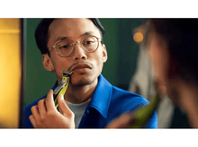 Charger l'image dans la galerie, Un homme se rase la moustache avec un rasoir électrique vert et noir, se regardant dans le miroir.