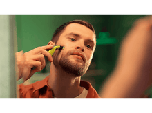 Charger l'image dans la galerie, Un homme se rasant le visage avec une tondeuse devant un miroir, chemise orange.