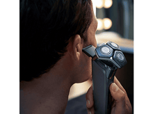 Charger l'image dans la galerie, Homme se rasant avec rasoir électrique, vue rapprochée. Fond: lumière floue.