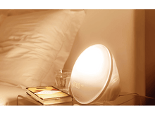 Charger l'image dans la galerie, Un réveil Philips blanc avec une lueur douce, et un livre et un verre d'eau à côté.