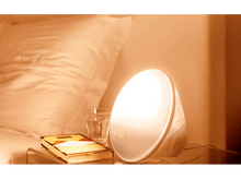 Charger l'image dans la galerie, Lampe de réveil Philips blanche avec l'heure 07h00 affichée, à côté d'un livre et d'un verre.