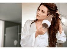 Charger l'image dans la galerie, Femme séchant ses cheveux avec un sèche-cheveux or rose, se regardant dans le miroir.