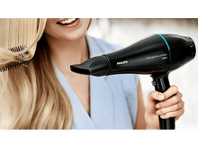 Charger l'image dans la galerie, Femme aux cheveux blonds utilisant un sèche-cheveux Philips noir et bleu.