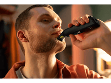 Charger l'image dans la galerie, Homme se rasant la barbe avec une tondeuse noire et jaune. Gros plan, arrière-plan flou.