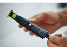 Charger l'image dans la galerie, Mains tenant une tondeuse Philips OneBlade noire. Vue rapprochée. Bouton marche/arrêt et voyants visibles.