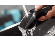 Charger l'image dans la galerie, L'eau coule sur un rasoir électrique noir. Une main tient le rasoir.