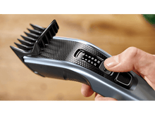 Charger l'image dans la galerie, La main d'une personne réglant les paramètres d'une tondeuse à cheveux grise et noire, gros plan.