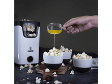 Charger l'image dans la galerie, Une personne verse du liquide jaune sur du pop-corn dans des bols blancs et noirs sur une planche de bois.