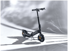 Charger l'image dans la galerie, Une trottinette gris foncé sur fond blanc avec effets de lumière.