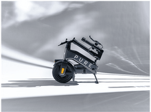 Charger l'image dans la galerie, Trottinette électrique pliée, noire et grise, garée sur une surface blanche. La trottinette est en studio.