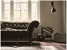 Charger l'image dans la galerie, Salon avec canapé vert, vélo et lampe. Un tapis et des enceintes sont également visibles.