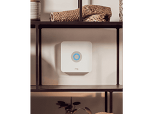 Charger l'image dans la galerie, Un système de sécurité Ring blanc est monté sur un mur. Il a un cercle bleu au centre. Des étagères au-dessus et en dessous contiennent des décorations.