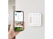 Charger l'image dans la galerie, Une main tient un téléphone affichant une application de sécurité. Un clavier blanc avec des chiffres et des symboles à côté.