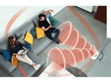 Charger l'image dans la galerie, Un couple est assis sur un canapé tandis qu'un aspirateur robot nettoie le sol. Des trajectoires de nettoyage rouges sont visibles.