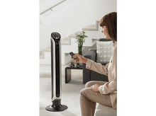 Charger l'image dans la galerie, Une femme utilise une télécommande pour un ventilateur haut, argenté et noir.