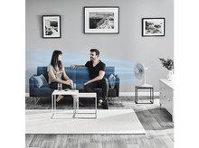 Charger l'image dans la galerie, Un couple assis sur un canapé avec un ventilateur soufflant de l'air.