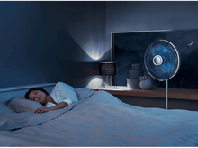 Charger l'image dans la galerie, Femme dormant dans un lit, avec un ventilateur à droite et une lampe.