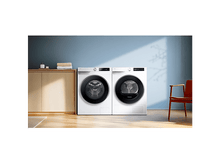 Charger l'image dans la galerie, Une machine à laver et un sèche-linge sont côte à côte. Une armoire en bois et une chaise orange sont en arrière-plan. Le mur est bleu.