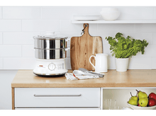 Charger l'image dans la galerie, Un comptoir de cuisine avec un cuiseur vapeur, une planche à découper, des ustensiles et des produits frais.