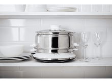 Charger l'image dans la galerie, Un cuiseur vapeur en acier inoxydable avec des verres à vin sur une étagère blanche.