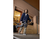 Charger l'image dans la galerie, Un jeune homme porte un scooter noir plié. Il marche dans une rue la nuit.