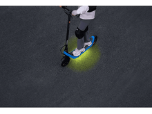 Charger l'image dans la galerie, Personne conduisant une trottinette bleue et noire sur une surface gris foncé. Les lumières de la trottinette brillent en vert.