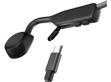 Charger l'image dans la galerie, Gros plan sur un casque à conduction osseuse, montrant le port de charge et un câble USB-C pour le chargement.