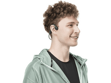 Charger l'image dans la galerie, Homme souriant portant un casque à conduction osseuse et une veste vert clair. Fond blanc.