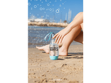 Charger l'image dans la galerie, Une main tenant une bouteille d'eau sur une plage avec des bulles dans l'air.