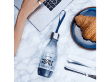 Charger l'image dans la galerie, Une bouteille sur une surface en marbre avec un ordinateur portable, un croissant et des couverts. Vue de dessus.