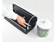 Charger l'image dans la galerie, Une personne utilisant une scelleuse alimentaire avec un récipient de verdure et un tuyau d'aspiration connecté.