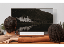 Charger l'image dans la galerie, Un couple regarde la télé avec un château. Une barre de son blanche est en dessous.