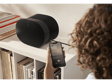 Charger l'image dans la galerie, Haut-parleurs noirs et téléphone jouant de la musique. Personne tenant le téléphone. Bibliothèque en arrière-plan.