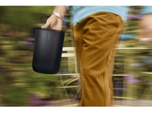 Charger l'image dans la galerie, Une personne tenant un haut-parleur cylindrique noir en marchant à l'extérieur.