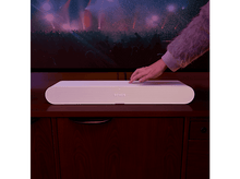 Charger l'image dans la galerie, Barre de son Sonos blanche sur une commode en bois, avec une main qui la touche.