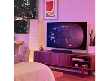 Charger l'image dans la galerie, Personne se relaxant dans une pièce avec TV et barre de son noire.