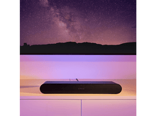 Charger l'image dans la galerie, Barre de son Sonos noire sous une TV. Le fond montre un ciel étoilé et un éclairage violet.