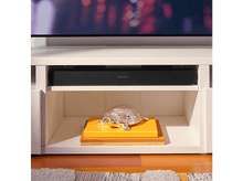 Charger l'image dans la galerie, Une barre de son Sonos noire sur une armoire blanche, avec des livres et une décoration de tortue argentée.